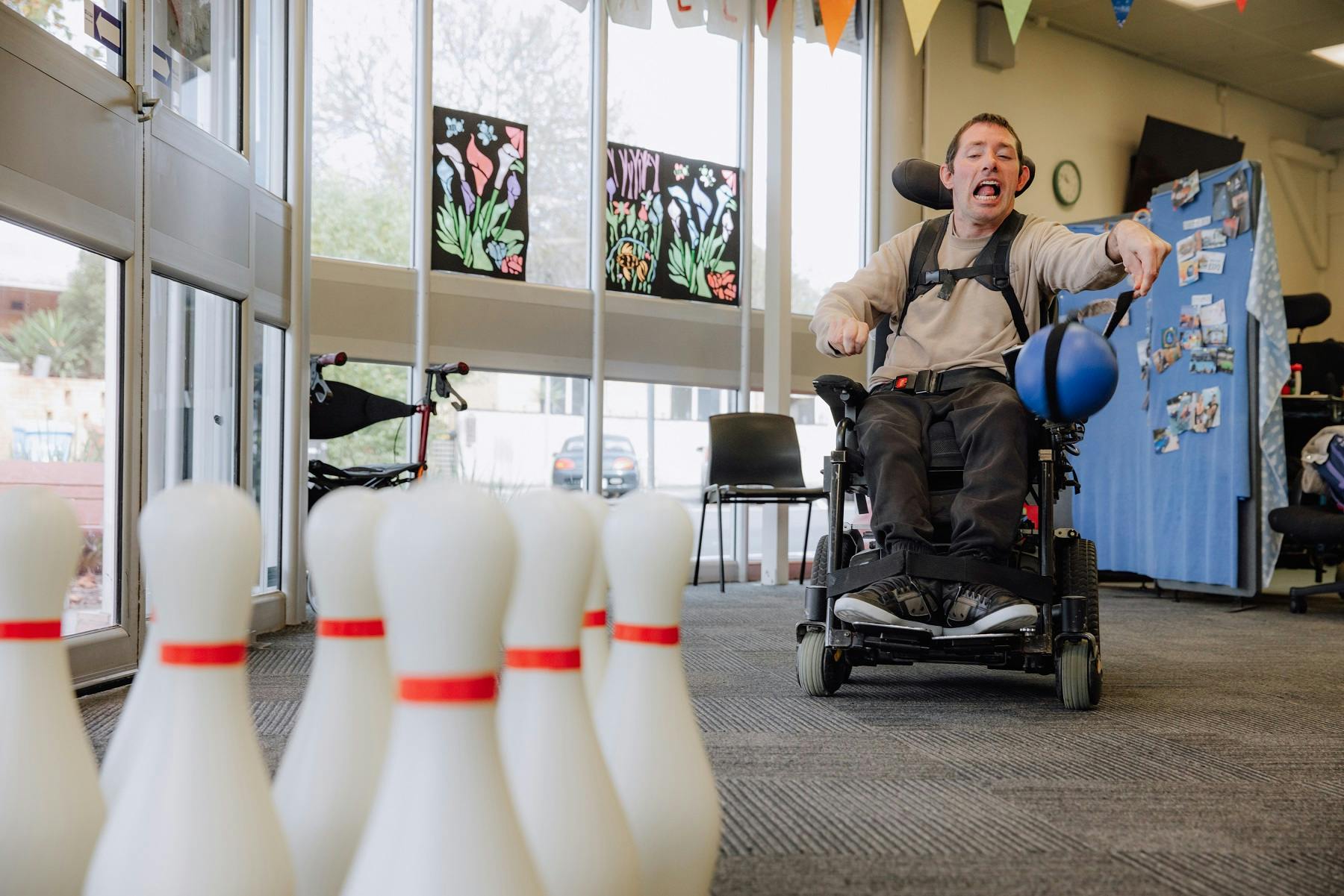 Image of a male playing tenpin bowling. He is smiling at the camera and using a wheelchair.