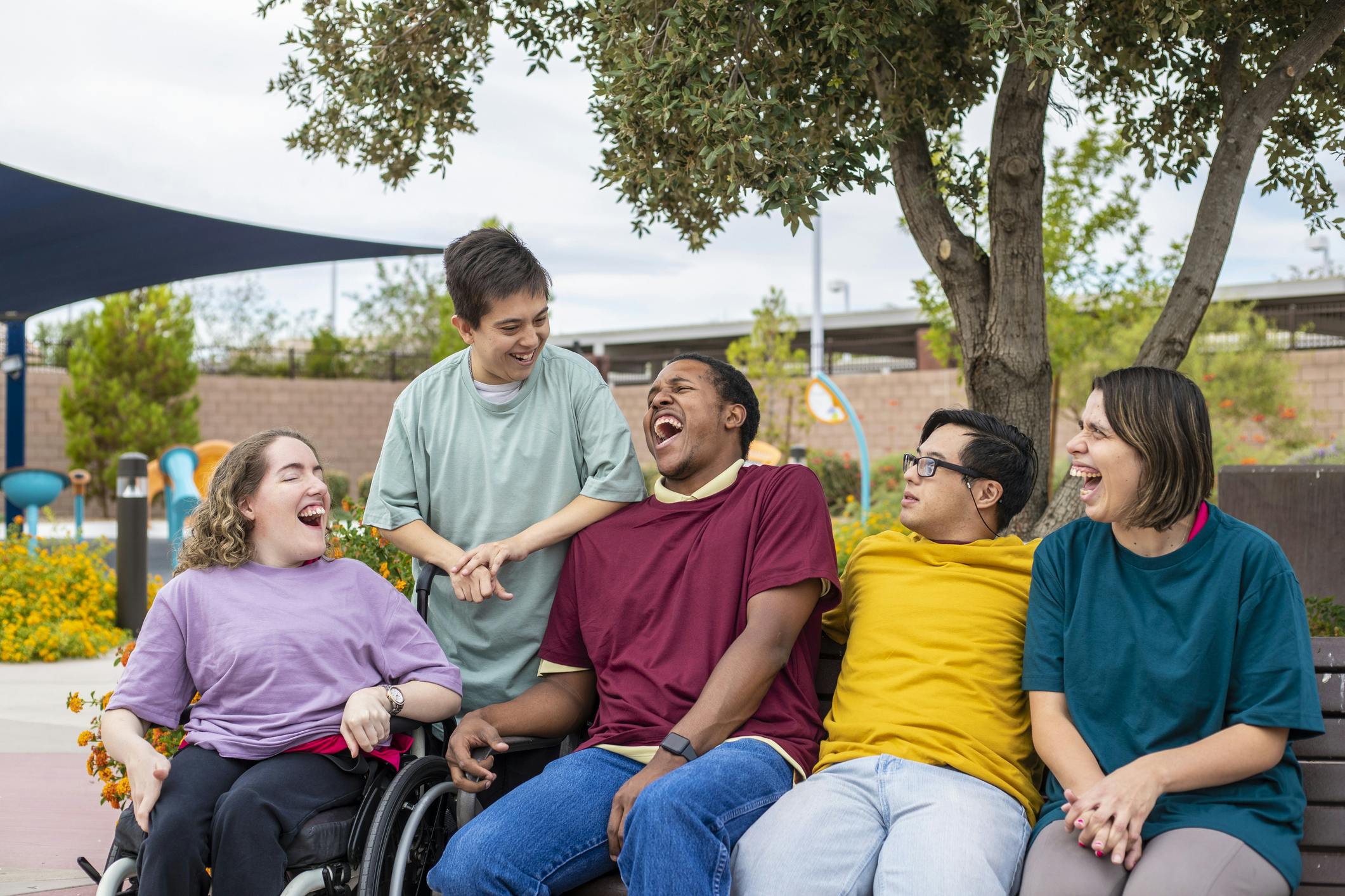 Image of a group of five young people sitting together, laughing and smiling. Two of the people have visible disabilities.