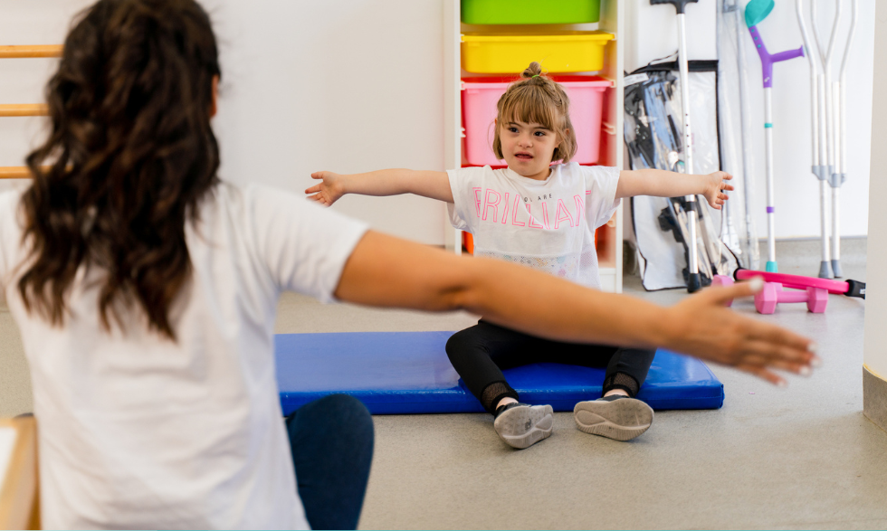 IMAGE: A Young child with arms stretched is working on their movement with a physiotherapist
