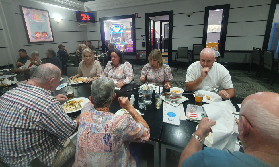 Clients, employees and their friends and family have gathered together at a table to have dinner at a local venue